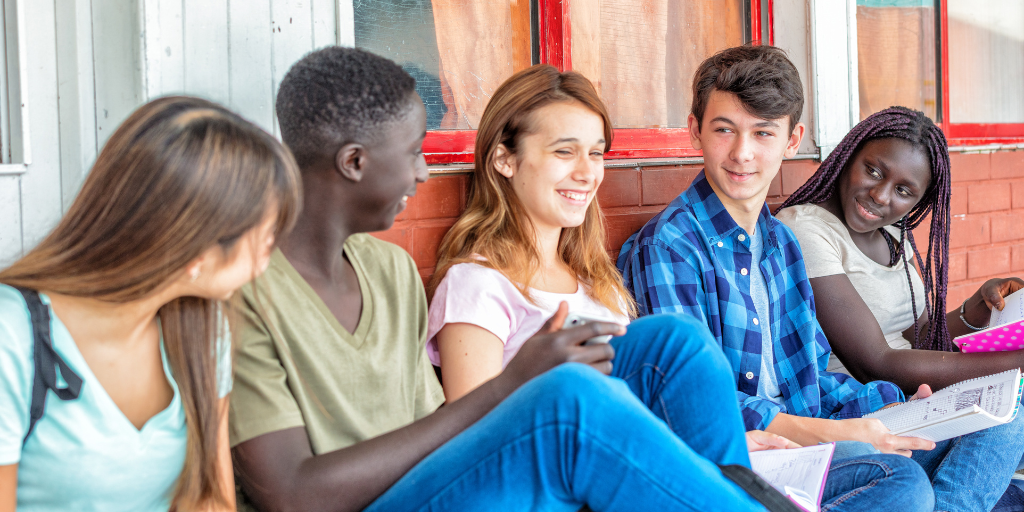 Photo of a groups of teens smiling and laughing together on a bench